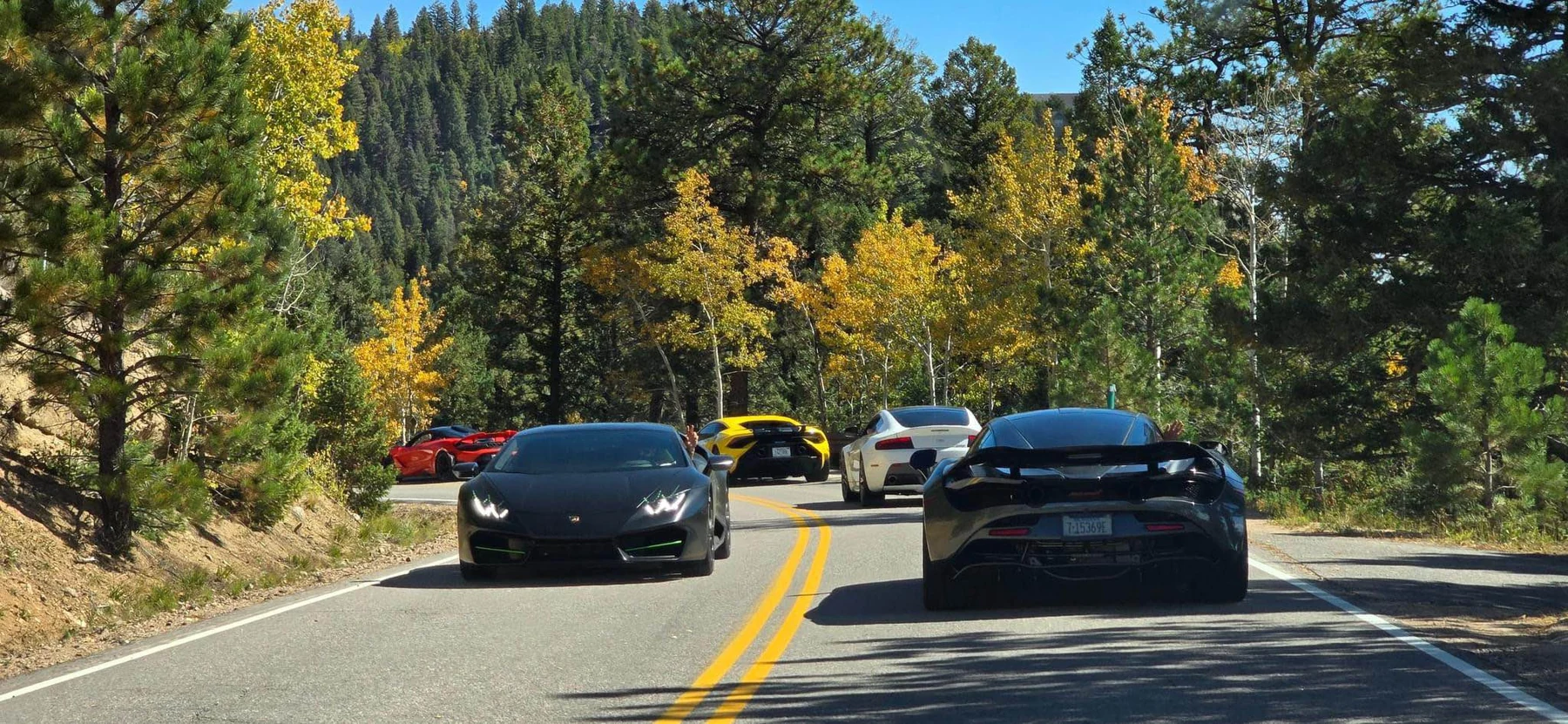 Exotic cars on a Colorado mountain road framed by autumn trees