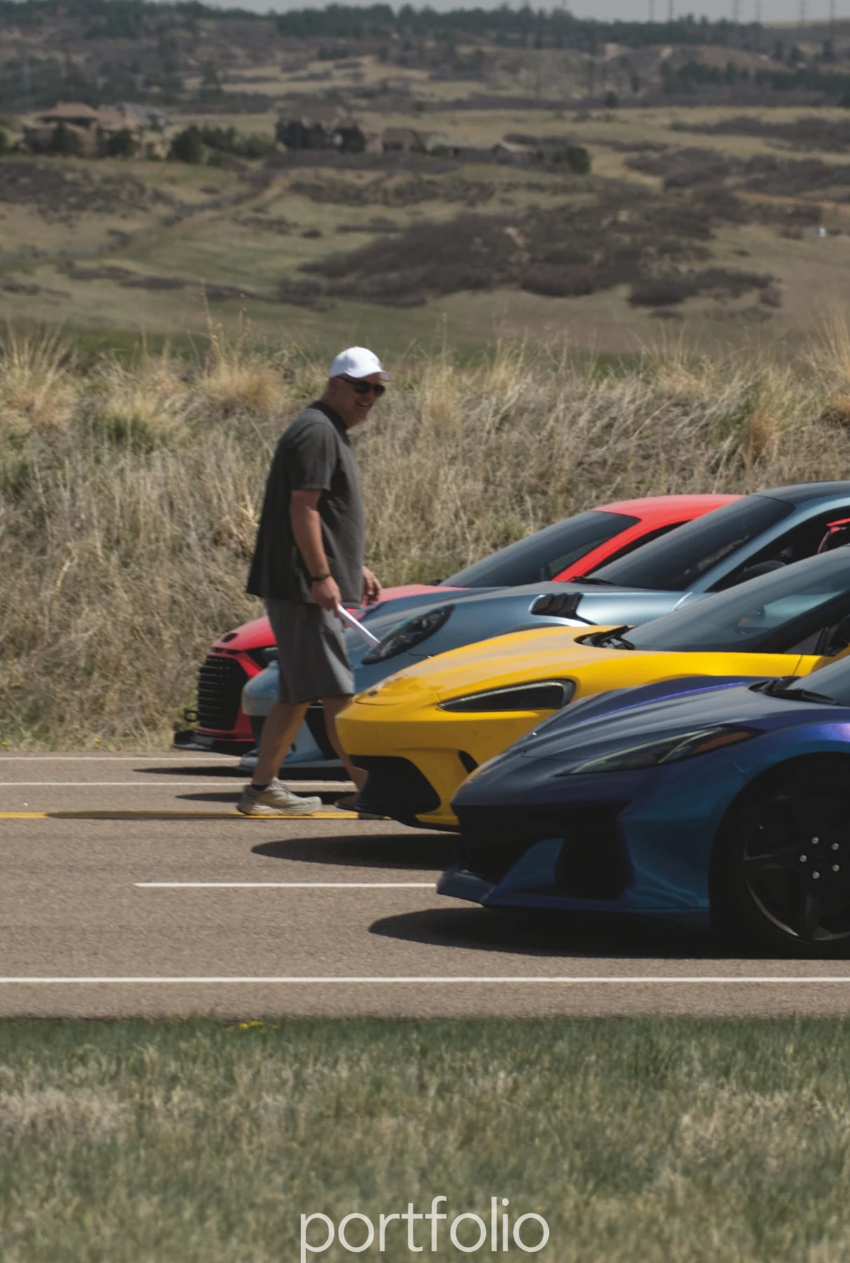 An attendee beside sports cars in a paddock; original watermark retained